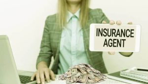 Businesswoman holding a sign that reads "Insurance Agent" with cash on the desk, symbolizing how insurance agents make money through commissions and earnings.