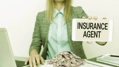 Businesswoman holding a sign that reads "Insurance Agent" with cash on the desk, symbolizing how insurance agents make money through commissions and earnings.