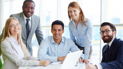 Group of professional employees smiling in a modern office setting, representing the positive work environment at the best insurance companies to work for.