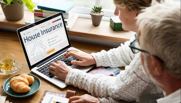 An elderly couple sitting at a table using a laptop to explore Honey Home Insurance options online, reviewing house insurance coverage details over breakfast with coffee and croissants.