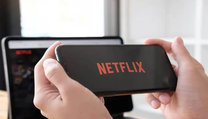 Learn How To Pay Netflix Via Mpesa Securely - Finsurancebiz A person holding a smartphone displaying the Netflix logo, symbolizing online streaming and digital subscriptions — How to Pay Netflix via Mpesa Securely.
