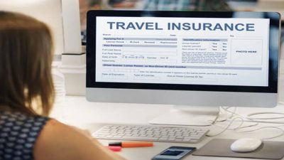 A woman sitting at her desk looking at a computer screen displaying an online travel insurance form — concept illustrating RACQ Travel Insurance application and coverage process for travellers.