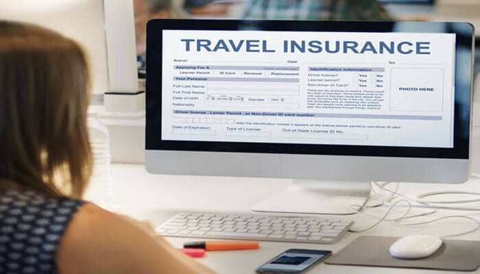 RACQ Travel Insurance Review: What Travellers Should Know - Finsurancebiz A woman sitting at her desk looking at a computer screen displaying an online travel insurance form — concept illustrating RACQ Travel Insurance application and coverage process for travellers.