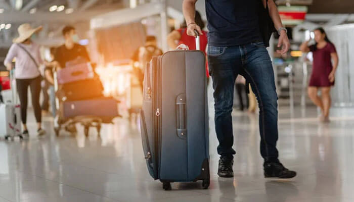 A traveler walking through an airport terminal pulling a suitcase, symbolizing the protection and peace of mind offered by RACQ Travel Insurance for both domestic and international trips.