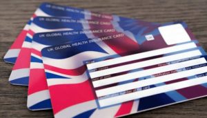 Close-up of multiple UK Global Health Insurance Card (GHIC) cards stacked on a wooden table, displaying the Union Jack design and blank information fields for cardholders.