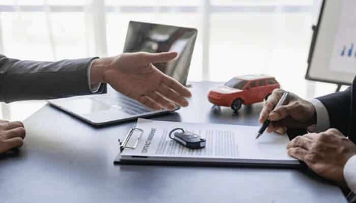 List of Common Insurance Types and What They Protect Against - finsurancebiz - Finsurancebiz Two people finalizing an insurance agreement at a desk, with a clipboard, car key, and model car visible, representing common insurance types such as auto insurance.