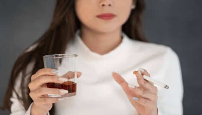 Top Reasons People Are Disqualified from Long-Term Care Insurance - finsurancebiz - Finsurancebiz A woman holding a glass of liquor and a cigarette, symbolizing lifestyle choices that can impact eligibility for long-term care insurance due to their effect on health.