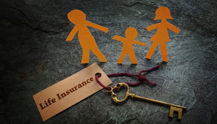 List of Common Insurance Types and What They Protect Against - finsurancebiz - Finsurancebiz Paper cutout silhouettes of a family—two adults and a child—on a dark surface beside a key and a tag labeled ‘Life Insurance,’ representing common insurance types and family financial protection.