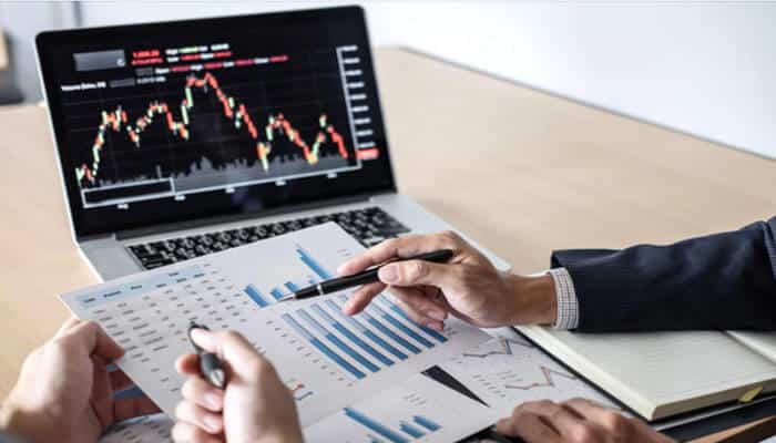 What Is Qualified Business Income Deduction- Explained In Detail - finsurancebiz - Finsurancebiz Two people analyzing financial data, with a focus on bar charts and graphs displayed on paper and a laptop screen, representing the process of calculating the Qualified Business Income Deduction (QBI)