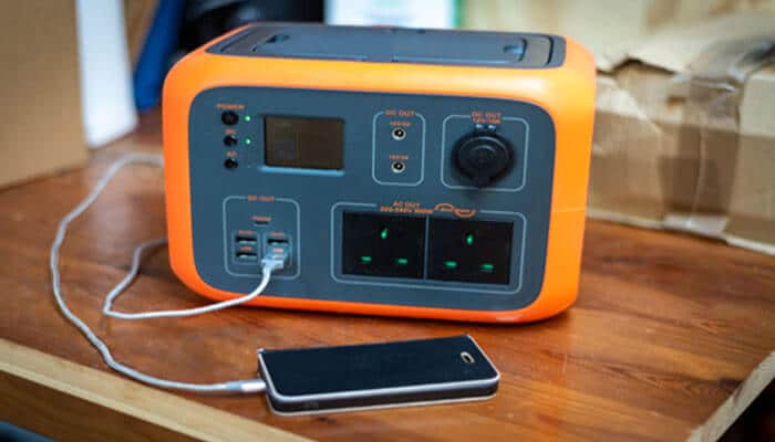 How to Get a Free Generator From the Government (2026 Guide) - finsurancebiz - Finsurancebiz Portable emergency backup power solutions setup showing a battery-powered power station charging a smartphone on a table.