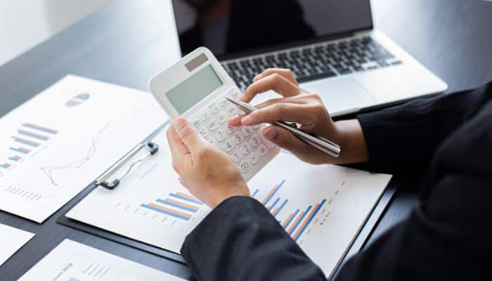 How Long Does a Tax Refund Take to Direct Deposit? 2026 IRS Timeline & Delays- finsurancebiz - Finsurancebiz How long does a tax refund take to direct deposit, shown with a taxpayer using a calculator beside a laptop and financial charts while reviewing refund timing.